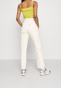 Top corto de punto amarillo claro con detalles texturizados, combinado con pantalones de pana color crema de pierna recta y bolsillos traseros. Zapatillas plateadas.