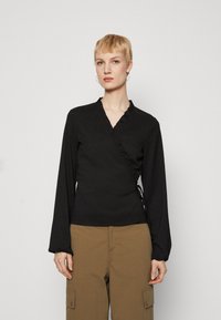 Top negru cu mâneci lungi, decolteu cu volane, material texturat și șnururi laterale ajustabile, asortat cu pantaloni cargo bej.