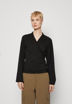 Black wrap top with long sleeves, ruffled neckline, textured fabric, and adjustable side ties, paired with beige cargo pants.