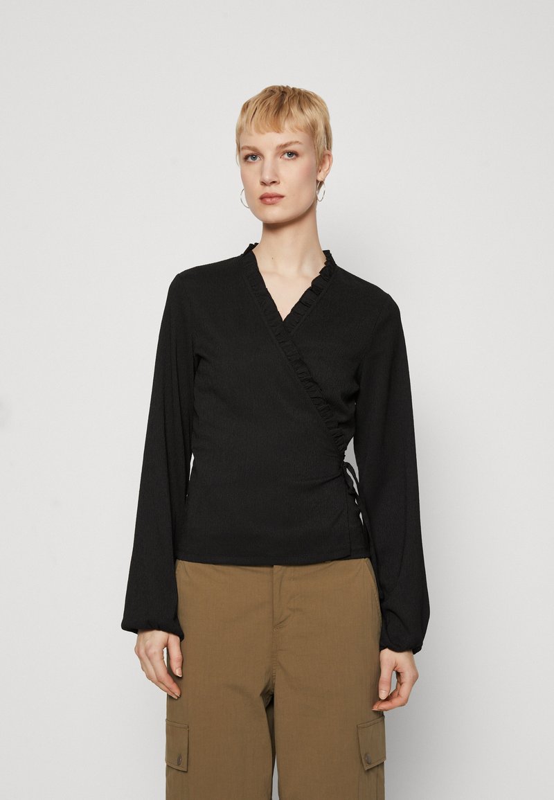 Top negru cu mâneci lungi, decolteu cu volane, material texturat și șnururi laterale ajustabile, asortat cu pantaloni cargo bej.