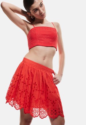 Top corto rosso con ricami intricati e spalline regolabili, abbinato a una gonna lunga fino al ginocchio con dettagli floreali ritagliati e una vita elasticizzata.