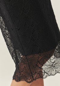 Material din dantelă neagră cu modele florale complexe și tiv ondulat. Textură moale cu detalii transparente vizibile.