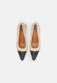 Bézs velúr magassarkú cipők fekete lakkbőrből készült hegyes orrral. Nyitott oldalakkal és sima belsővel rendelkeznek. Minimalista dizájn elegáns színkontraszttal.