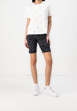 Hvid kortærmet top med udskårne blomstermotiver kombineret med sorte cykelshorts med leopardprint og hvide sneakers.
