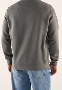 Sudadera gris de manga larga, con puños acanalados y cuello redondo, combinada con vaqueros de mezclilla azul claro. Diseño sencillo y casual.