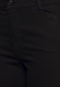 Musta denimmit housut, joissa on sileä, mattapintainen rakenne. Niissä on nappisuljenta, vyölenkit ja oikealla puolella oleva etutasku.