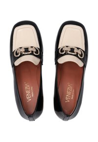 Zwarte en crèmekleurige loafers met een glanzende afwerking, voorzien van een metallic kettingaccent aan de voorkant en een gestructureerd leren ontwerp.