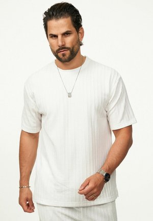 White short-sleeve shirt with textured vertical stripes, round neckline, and relaxed fit. Silver necklace and wristwatch visible.