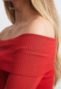 Haut rouge côtelé décolleté bardot avec une large bande au niveau du col, présentant une texture lisse et une silhouette ajustée le long du corps.