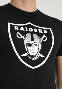 T-shirt in cotone nero con un grande logo bianco dei Raiders raffigurante un personaggio stilizzato con un casco e una benda sull'occhio.
