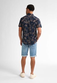 Camicetta a maniche corte blu navy con motivo floreale beige, abbinata a pantaloni corti di jeans leggeri azzurri arrotolati. Indossata con sneakers bianche.
