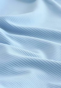 Tissu bleu clair avec une fine texture côtelée verticale, délicatement plié et créant de douces vagues et ombres.