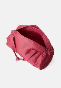 Rosa duffelväska med en texturerad yta, dubbla handtag och ett dragkedjeöppning. Inuti finns en slät foder med en extra ficka.