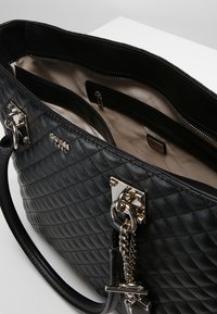 Gepolsterte schwarze synthetische Lederhandtasche mit silberner Hardware, ausgestattet mit zwei Innenfächern und einem einzelnen oberen Reißverschlussverschluss.