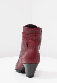 Botín de cuero rojo hasta el tobillo con punta redonda, superficie texturizada, cremallera lateral y tacón medio. Presenta costuras sutiles y una suela resistente.