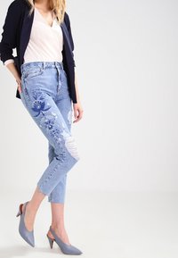 Světle modré, oprané džíny s květinovou výšivkou na jedné nohavici. Kombinováno s bílou blůzou a šedými lodičkami.