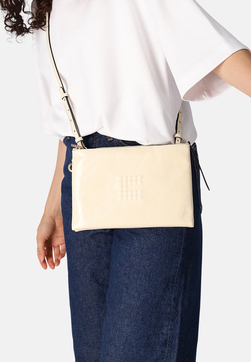 Crème-kleurige leren crossbodytas met gestructureerd oppervlak en geperst logo. Voorzien van verstelbare riem en ritssluiting. Rechthoekige vorm.