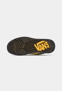 Semelle d'une chaussure Vans noire et jaune avec motifs de bande de roulement en losange et en ligne et grand logo Vans jaune près du talon.