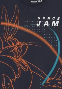 Tmavě námořnické tričko s oranžovým obrysem postavy a textem "SPACE JAM" v bílé barvě, doplněné geometrickými motivy v světlé modré a čtverci.