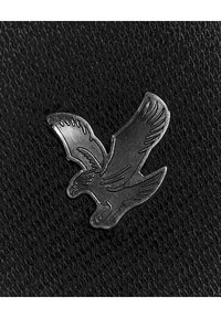 Épingle métallique en forme d'oiseau en vol avec des ailes gravées en détail sur un fond en cuir noir texturé.
