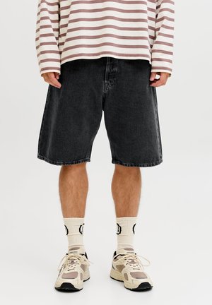 Pantalones cortos de mezclilla negros con un ajuste holgado, dobladillo sin rematar, combinados con una camiseta de manga larga a rayas, calcetines crema y zapatillas beige.