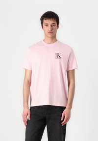 T-shirt en coton rose clair avec un col rond, des manches courtes et un petit logo Calvin Klein dans le coin supérieur gauche.