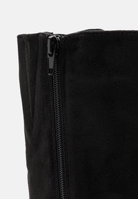 Sort semsket støvel med glinsende svart glidelås, med en jevn tekstur og et høyt, strukturert design.