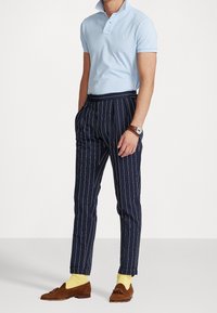 Světle modrá polokošile s límečkem, kalhoty s námořnickými pruhy, žluté ponožky a hnědé mokasíny. Výrazné pruhy na kalhotách, neformální styl.