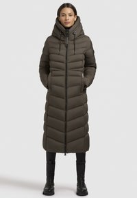 Giacca puffer verde oliva con colletto alto, design a cuciture verticali, chiusura con zip e tasche laterali. Presenta una silhouette lunga e slim.