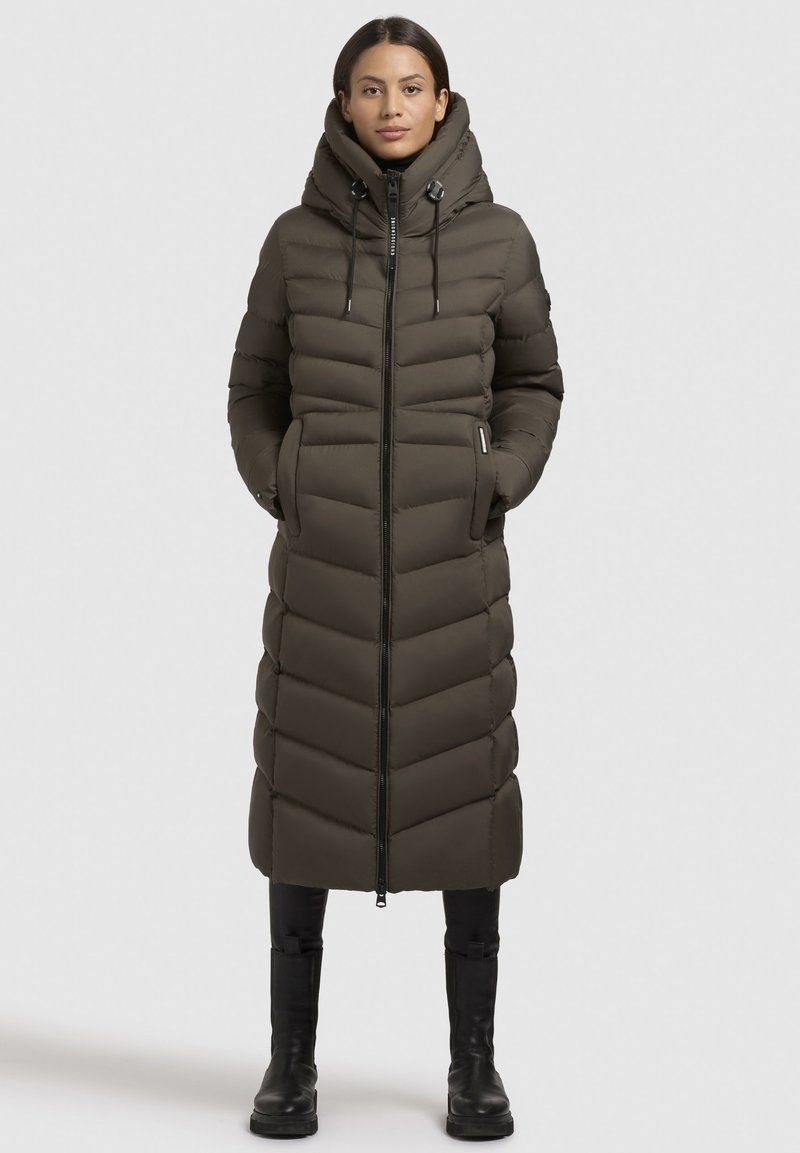 Giacca puffer verde oliva con colletto alto, design a cuciture verticali, chiusura con zip e tasche laterali. Presenta una silhouette lunga e slim.