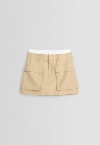 Jupe cargo beige avec taille élastique blanche, dotée de deux grandes poches avant, forme ajustée et texture de tissu lisse.