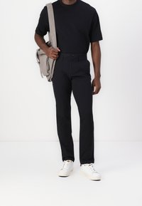 Sort T-shirt med korte ærmer, kombineret med mørke bukser og hvide sneakers. Grå buddeltaske hængende over skulderen. Simpelt, minimalistisk design.