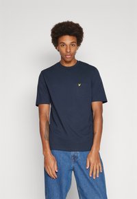 T-shirt in cotone blu navy con collo rotondo, maniche corte e una tasca sul petto che presenta un piccolo logo giallo. Tessuto liscio.
