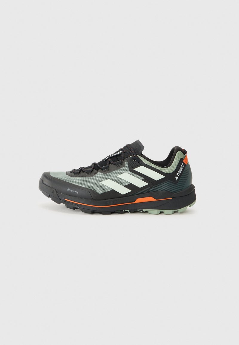 Lahka tekaška čevlja za trail s sivim in črnim mrežastim zgornjim delom, oranžnimi poudarki in robustnim podplatom za oprijem. Vodoodporna Gore-Tex podloga.