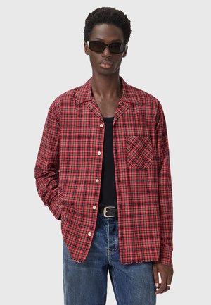 Red and black plaid button-up shirt with a chest pocket, worn over a black tank top. Made of woven fabric, has a relaxed fit and long sleeves.