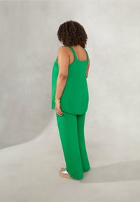 Grön ärmlös topp kombinerad med vida gröna byxor, tillverkade av mjukt material. Skorna är silverfärgade ballerinor.