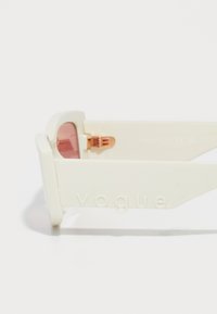 Hvite rektangulære solbriller med rosa linser og "vogue" preget på den tykke buen, vist i nære opptak mot en hvit bakgrunn.