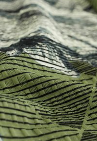 Tissu présentant un motif abstrait vert avec des lignes et textures noires, mettant en valeur une surface tissée douce avec des textures et formes variées.