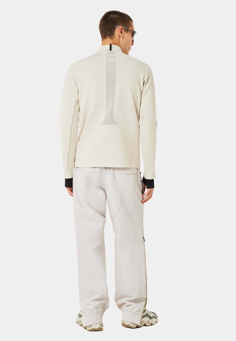 Light-colored, textured long-sleeve top with a large graphic on the back, paired with light pants and patterned footwear.