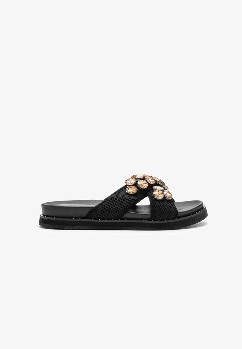 Sandales noires à lanières en maille entrecroisées ornées de grandes gemmes de couleur ambre et de petits clous autour de la semelle.