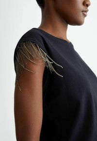 Top corto a maniche corte nero con dettagli in frange metalliche sulle spalle, realizzato in tessuto morbido con vestibilità rilassata e scollatura rotonda.
