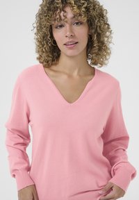 Maglione rosa con scollatura a V e maniche lunghe. Presenta una texture morbida e dettagli a costine nei polsini.