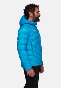 Giacca isolata blu con cappuccio, caratterizzata da un design a rombi trapuntato, due tasche con zip e una texture liscia e lucida.