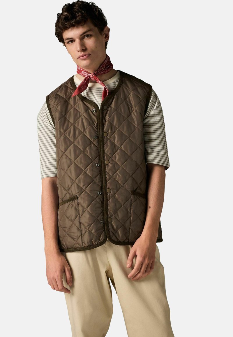Brown quilted vest with a trim, featuring snap buttons and two side pockets, worn over a striped shirt, complemented by a red bandana.