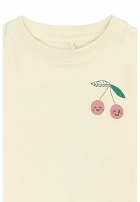 Krämfärgad t-shirt med kort ärm som har en grafisk bild av två rosa körsbär med leende ansikten och gröna blad på vänster sida.