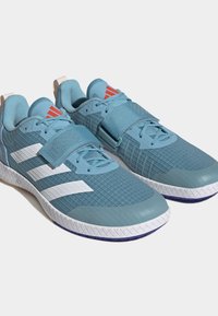 Baskets de sport bleues avec une tige en maille texturée, des rayures blanches, une sangle Velcro et une semelle en caoutchouc contrastante.