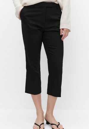 Femme portant un pantalon noir coupé court avec des poches latérales, associé à des sandales à talons ouvertes noires et un pull crème.