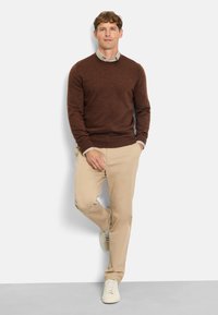 Brauner Strickpullover mit Rundhalsausschnitt, kombiniert mit beigen Chinos und weißen Sneakern. Das Outfit hat eine lässige und entspannte Passform.