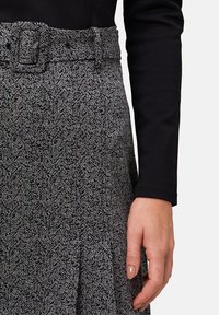 Jupe à motif pied-de-poule en noir et blanc, dotée d'une large ceinture avec une boucle rectangulaire. Le matériau semble texturé et tissé.