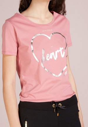 Roze katoenen T-shirt met een zilveren hartafbeelding en het woord "heart" erin. Korte mouwen en een ronde halslijn.